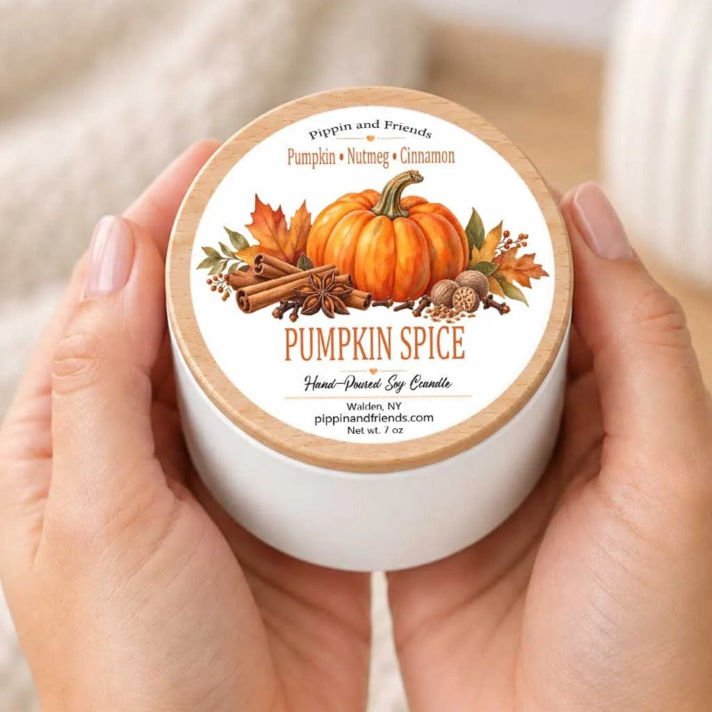 A person's hands holding a white container with a label featuring an illustration of a pumpkin and fall-themed spices.