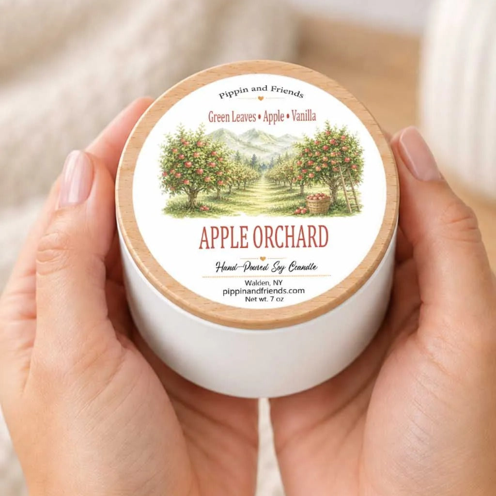 A person's hands holding a white container with a label that features an illustration of an apple orchard.