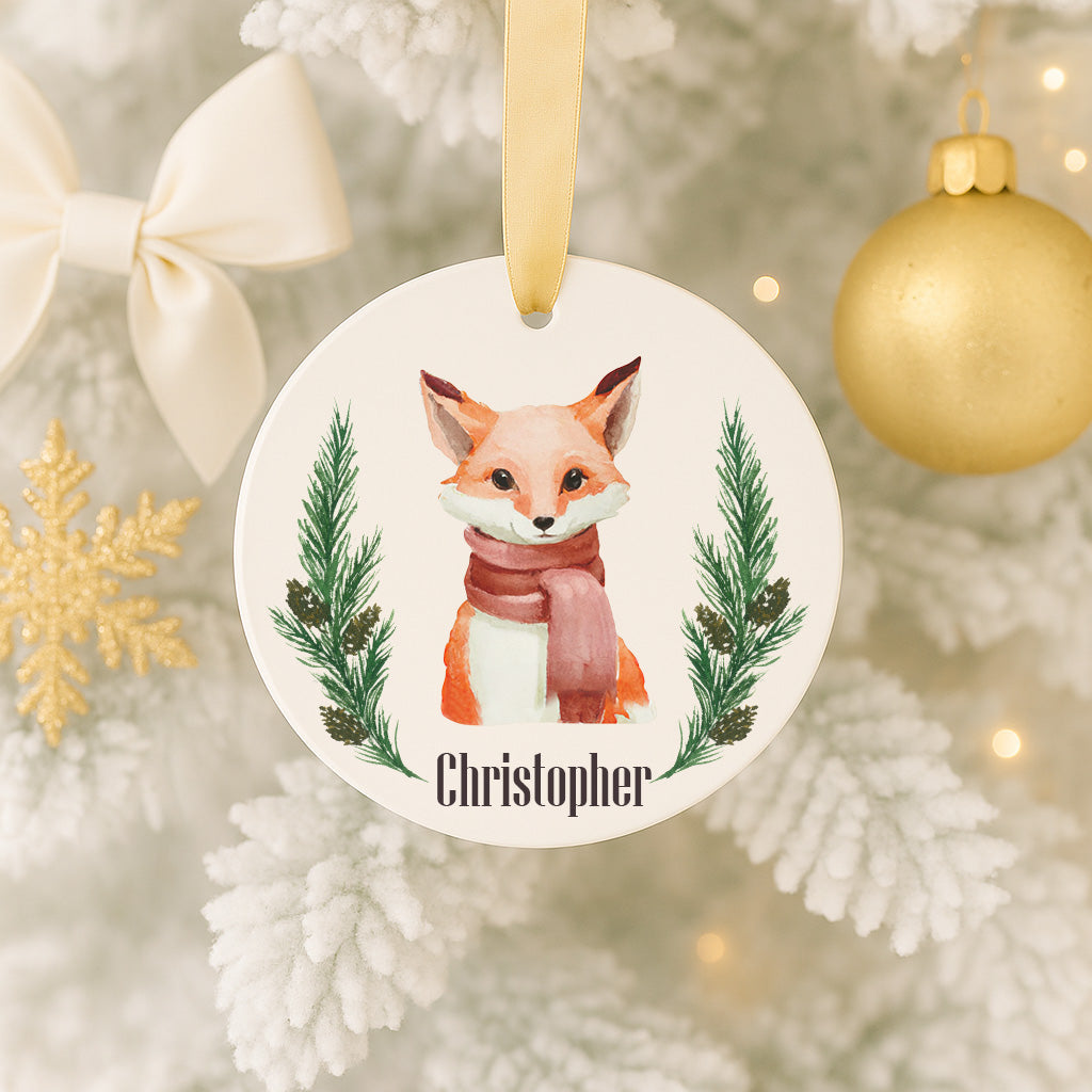 A white ornament with a fox wearing a red scarf and surrounded by pine branches, with the name "Christopher" written on it.