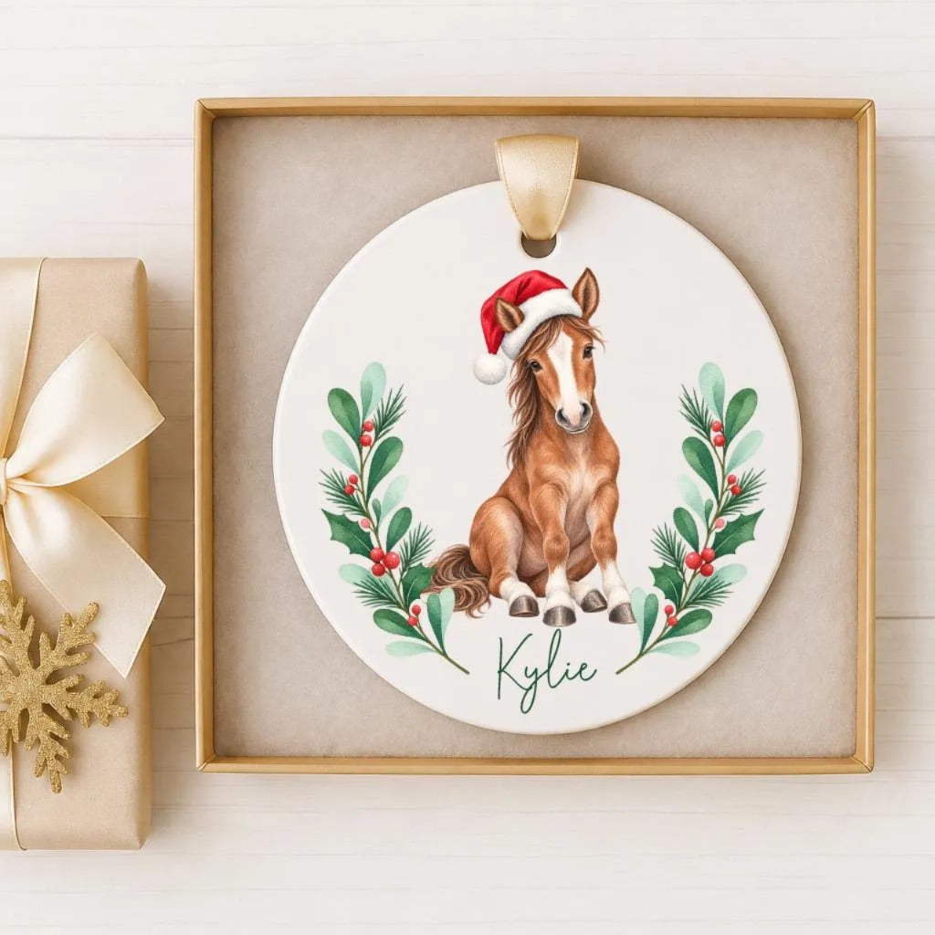 A ceramic ornament featuring a horse wearing a Santa hat, surrounded by a wreath of holly and berries, with the name " Kylie" written on it.