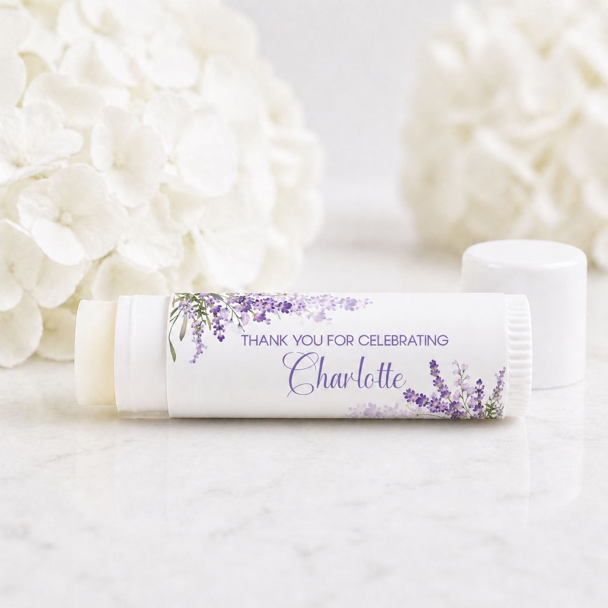 Set of 12 personalized lavender lip balm favors with purple floral labels reading thank you for celebrating Charlotte on white tubes
