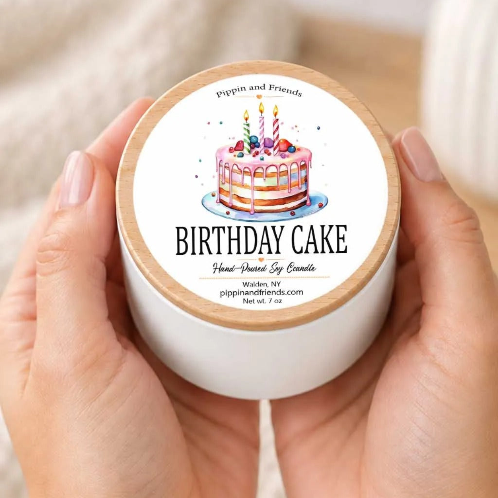A person's hands holding a white container with a label that features an illustration of a birthday cake with candles.