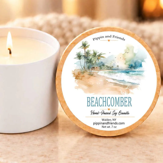 A white candle with a label that reads "Beachcomber" sits next to a lit candle on a table.