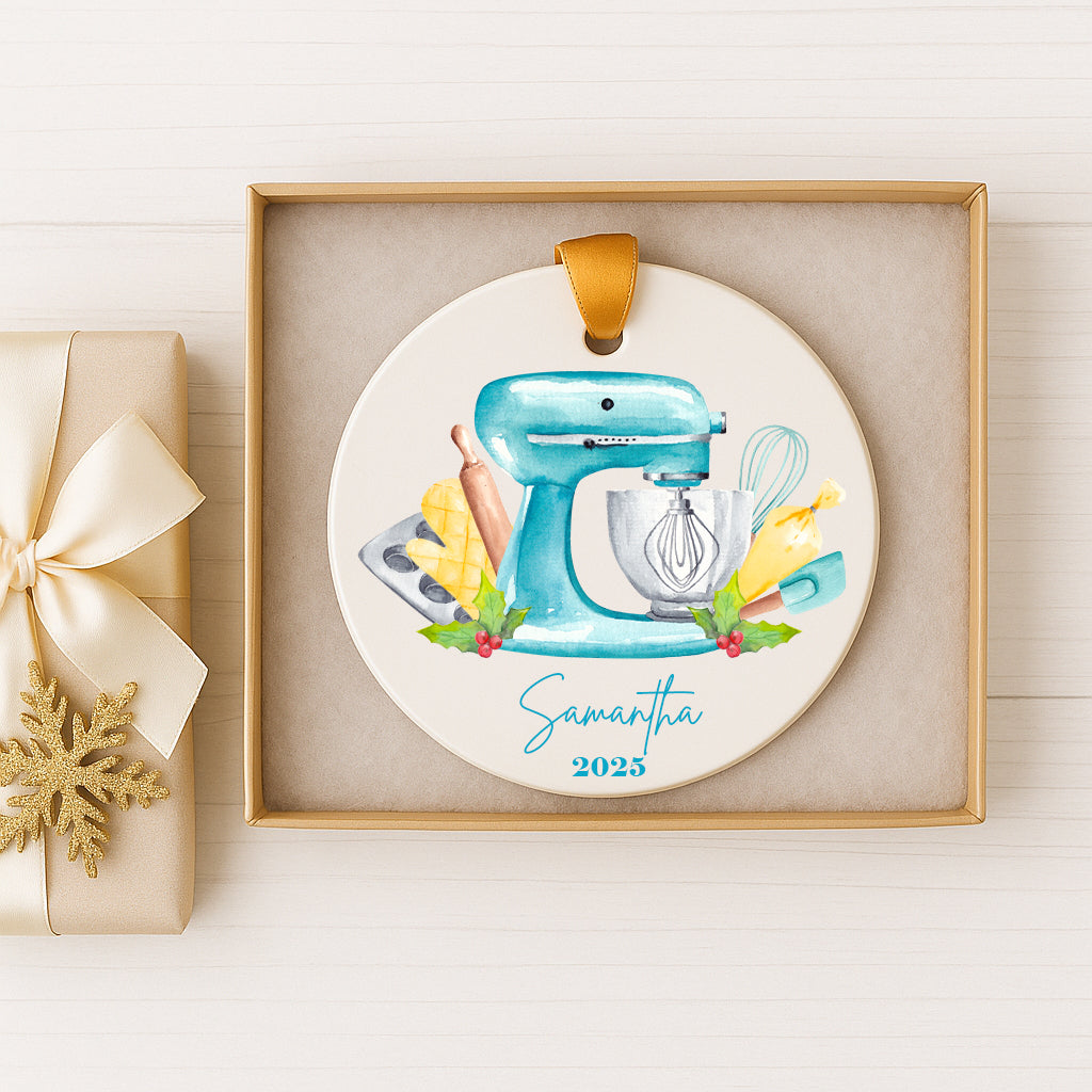 A decorative ornament featuring a blue mixer surrounded by kitchen utensils, such as a whisk and a rolling pin, with the name "Samantha" and the year "2025" displayed.
