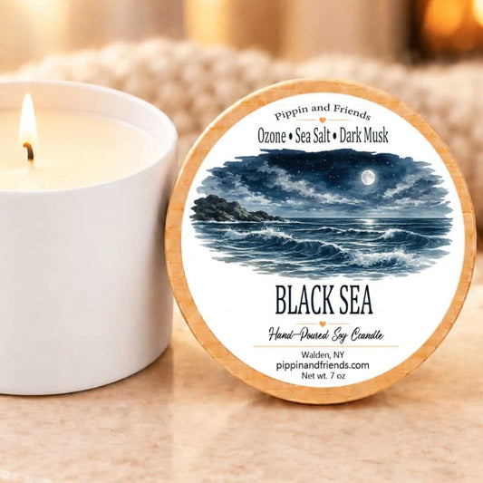 a white candle next to a wooden lid with a label that depicts a seascape with a full moon and waves.