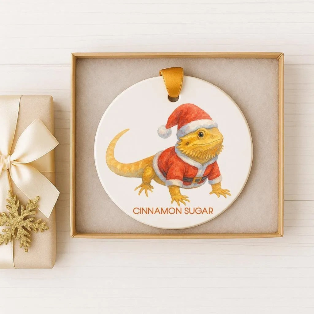 A ceramic ornament featuring a bearded dragon wearing a Santa hat, with the text "CINNAMON SUGAR" printed on it.