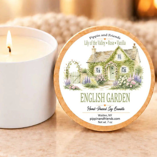 a white candle with a label that reads "English Garden" and "English Garden by Candle", placed next to a white candle holder.