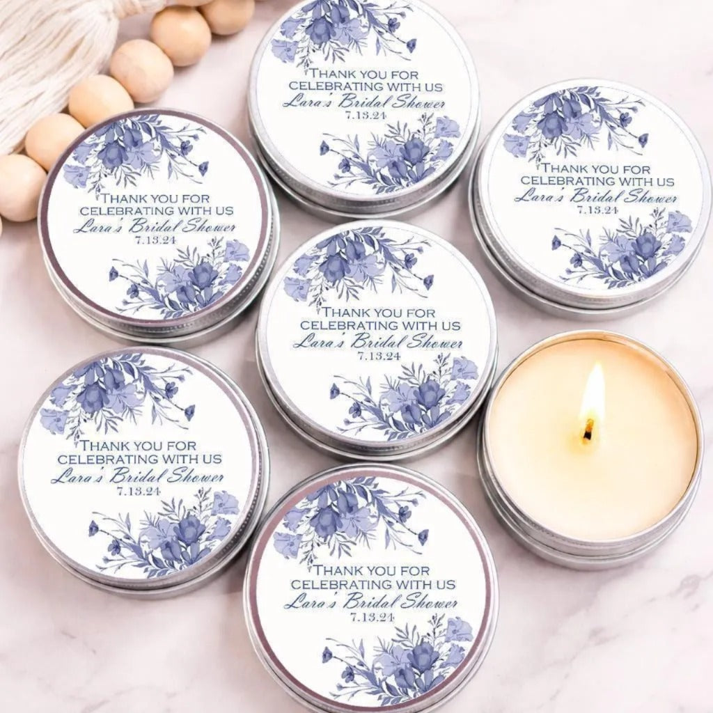 a collection of six silver tins arranged on a marble surface, each with a label that reads "Thank you for celebrating with us" and "Lara's Bridal Shower 7.13.21". The tins are arranged in a circular pattern, with one candle in the center.