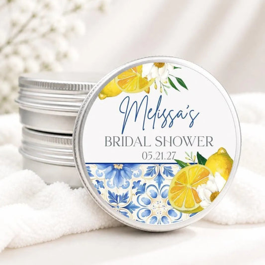 A round tin lid with a label that says "Melissa's BRIDAL SHOWER 05.21.27" and features a floral design with yellow and white flowers and lemon slices.