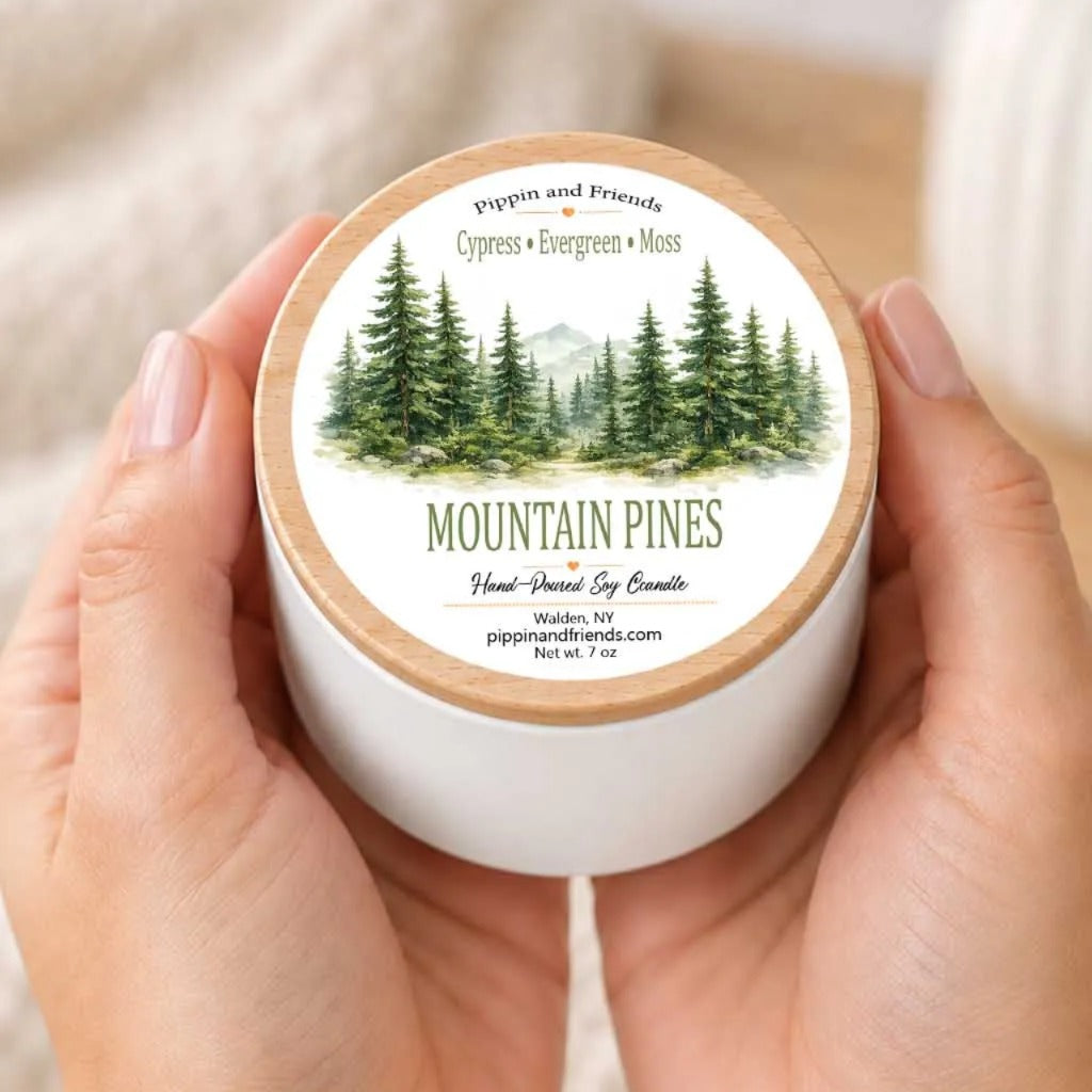 A person's hands holding a white container with a label featuring a forest scene and the text "Mountain Pines" and "Pippin and Friends" printed on it.