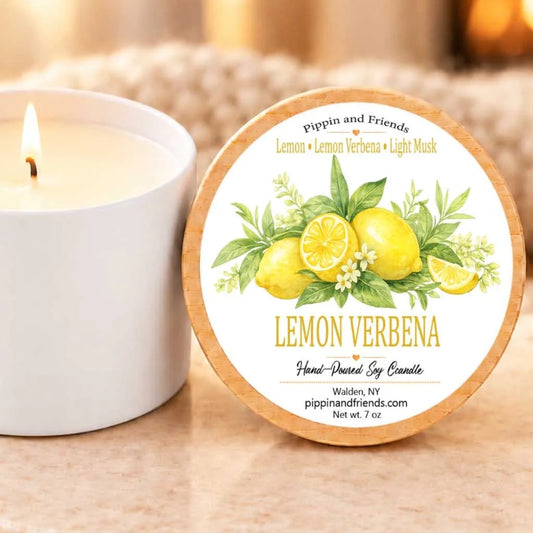 A white candle with a label that reads "Lemon Verbena" and "Hand-Drenched Soy Candle" next to it.