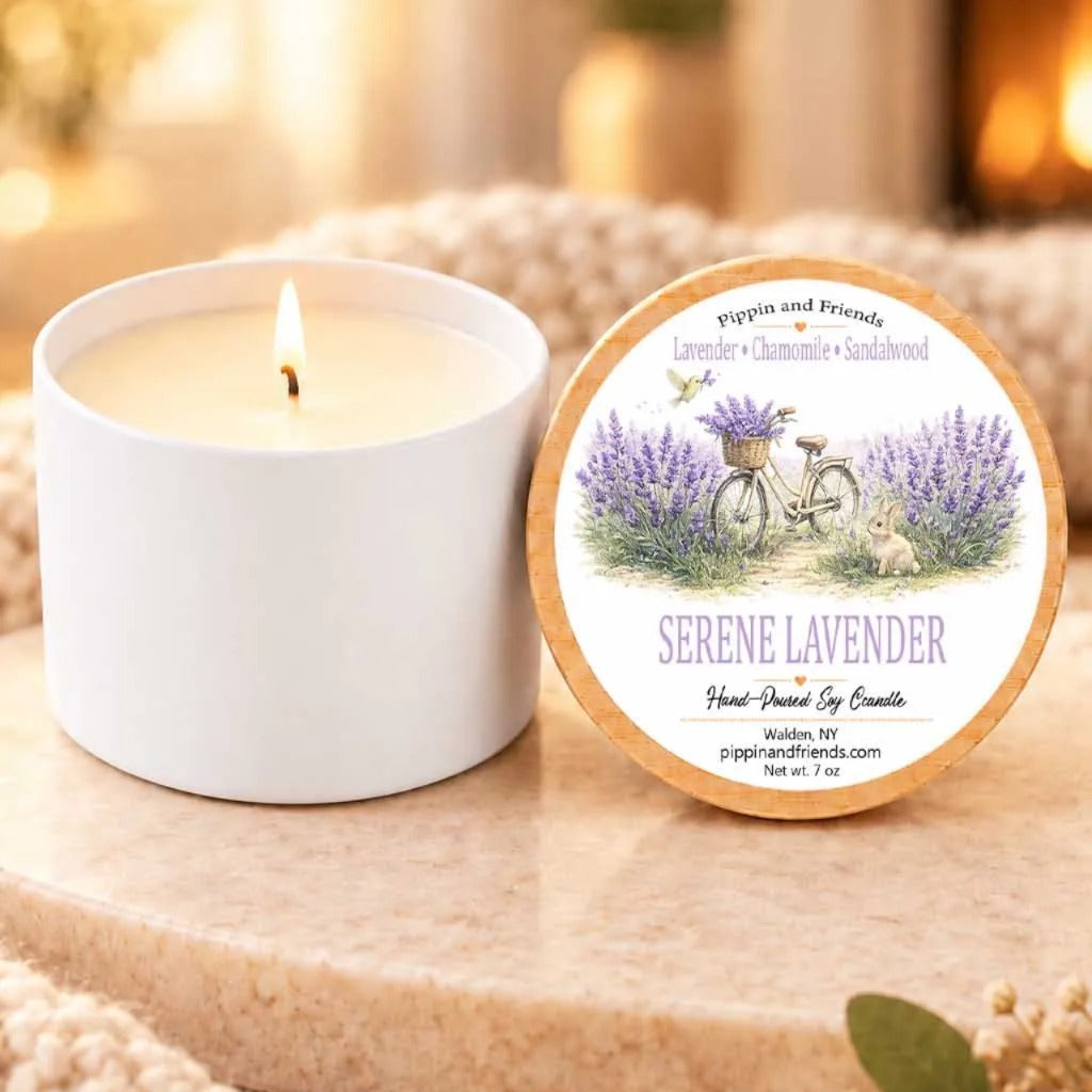 a white candle with a label that reads "Serene Lavender" and "Pippin and Friends" next to it. The candle is placed on a wooden surface, and there is a small plant or flower nearby.