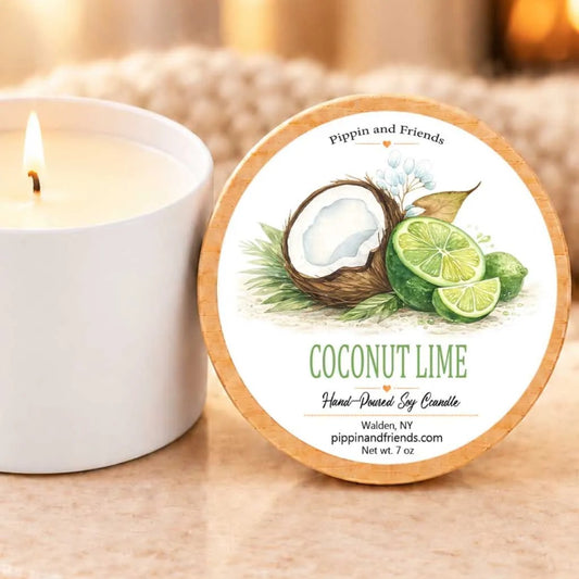 a white candle with a label that reads "COCONUT LIME Hand-poured Soy Candle" and " Walden, NY pippinandfriends.com net wt 7 oz". The candle is placed next to a white candle holder, creating a cozy and inviting scene.