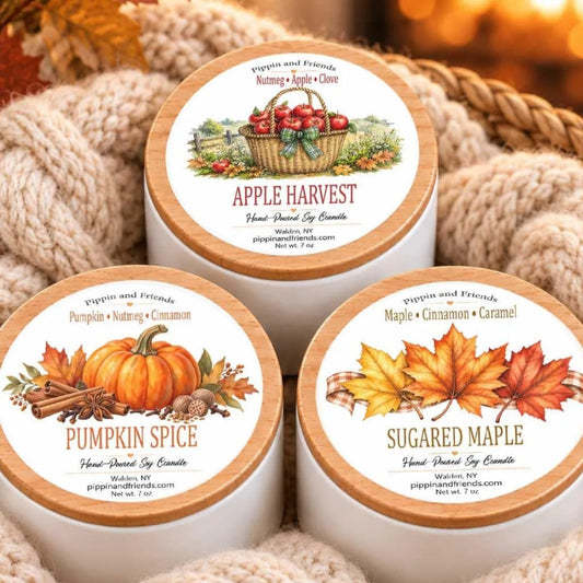 three white candle containers with autumn-themed labels, each containing a different scent.