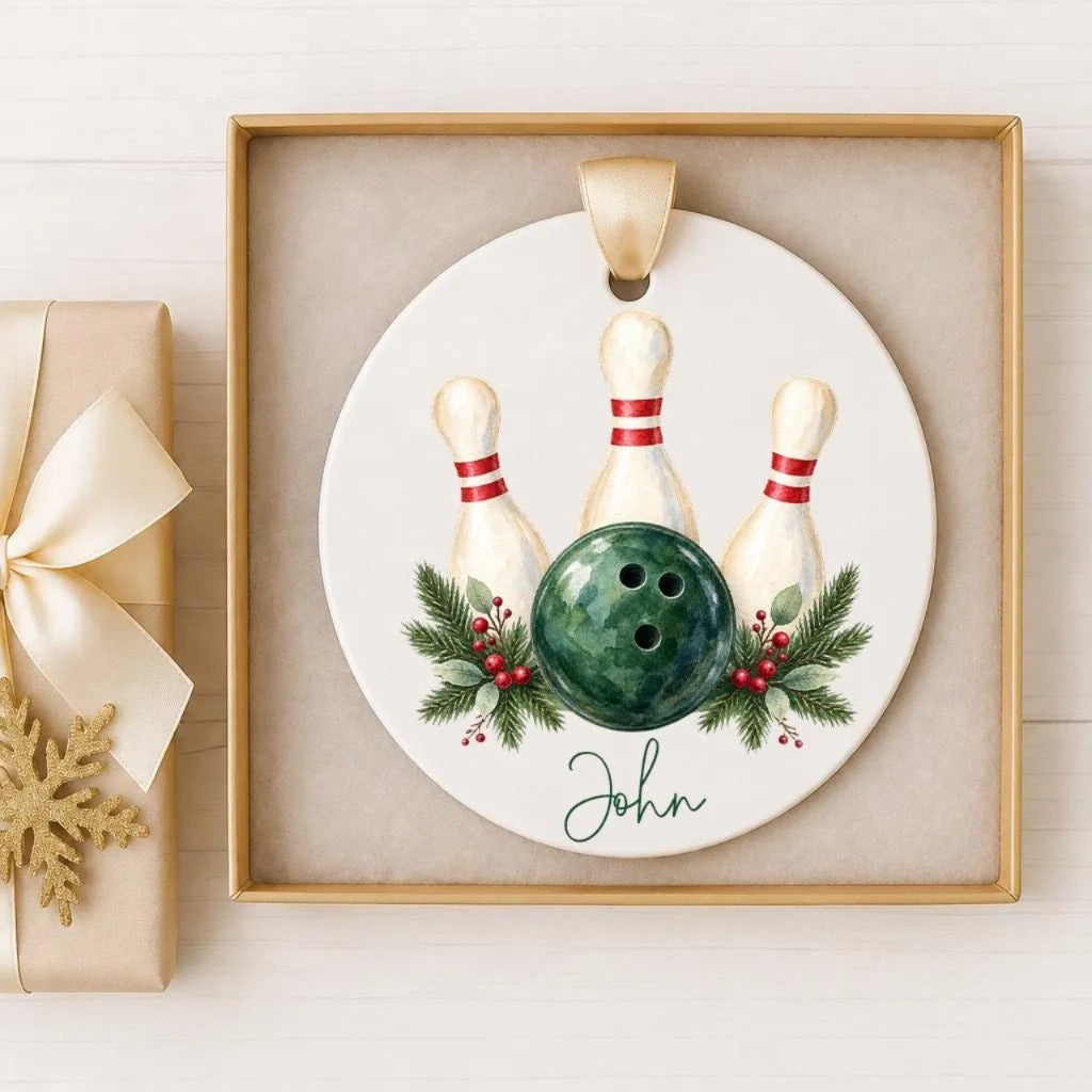 A white ornament with a bowling ball and three pins, surrounded by greenery and red berries, is displayed in a gold frame.