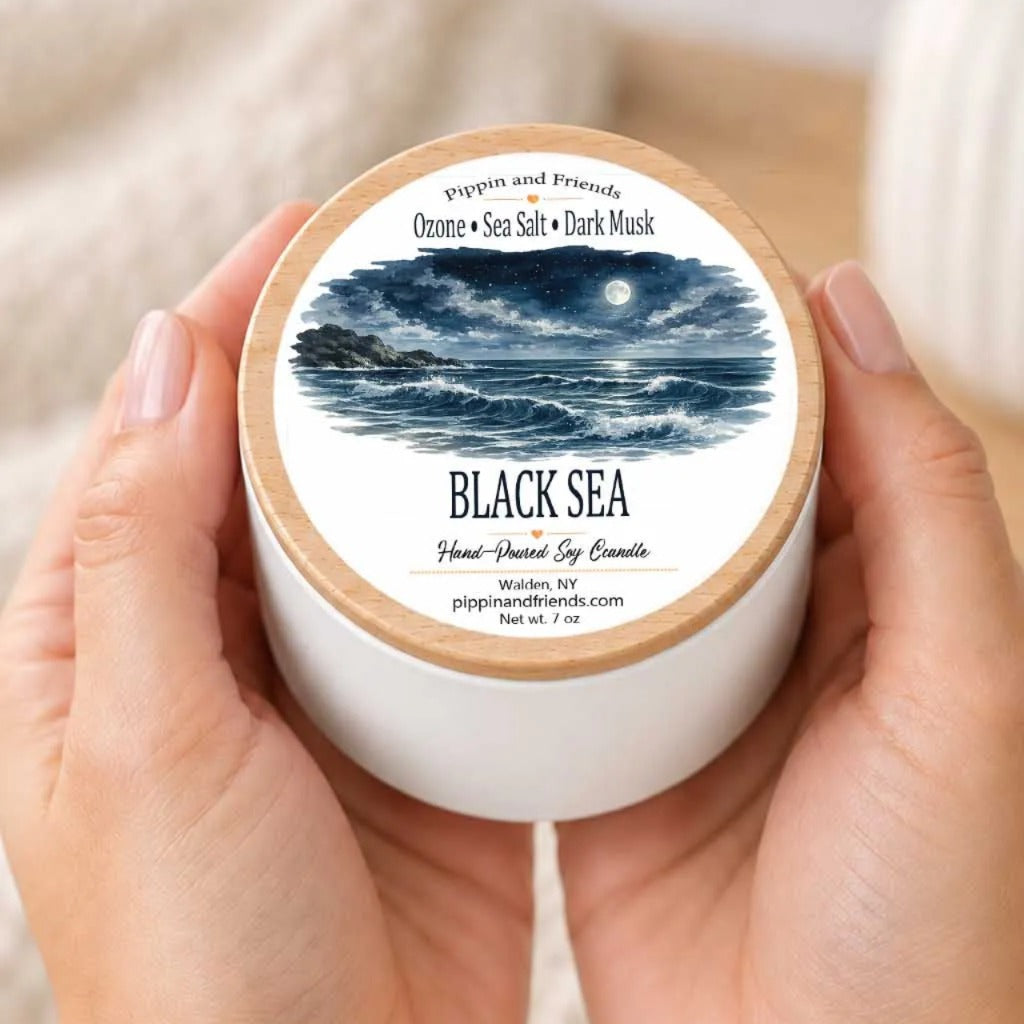 A person's hands holding a white container with a label that features an illustration of a night sky and ocean.