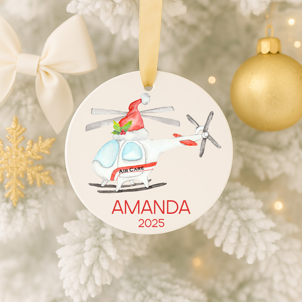 A white Christmas ornament with a helicopter and a red ribbon, hanging on a tree.