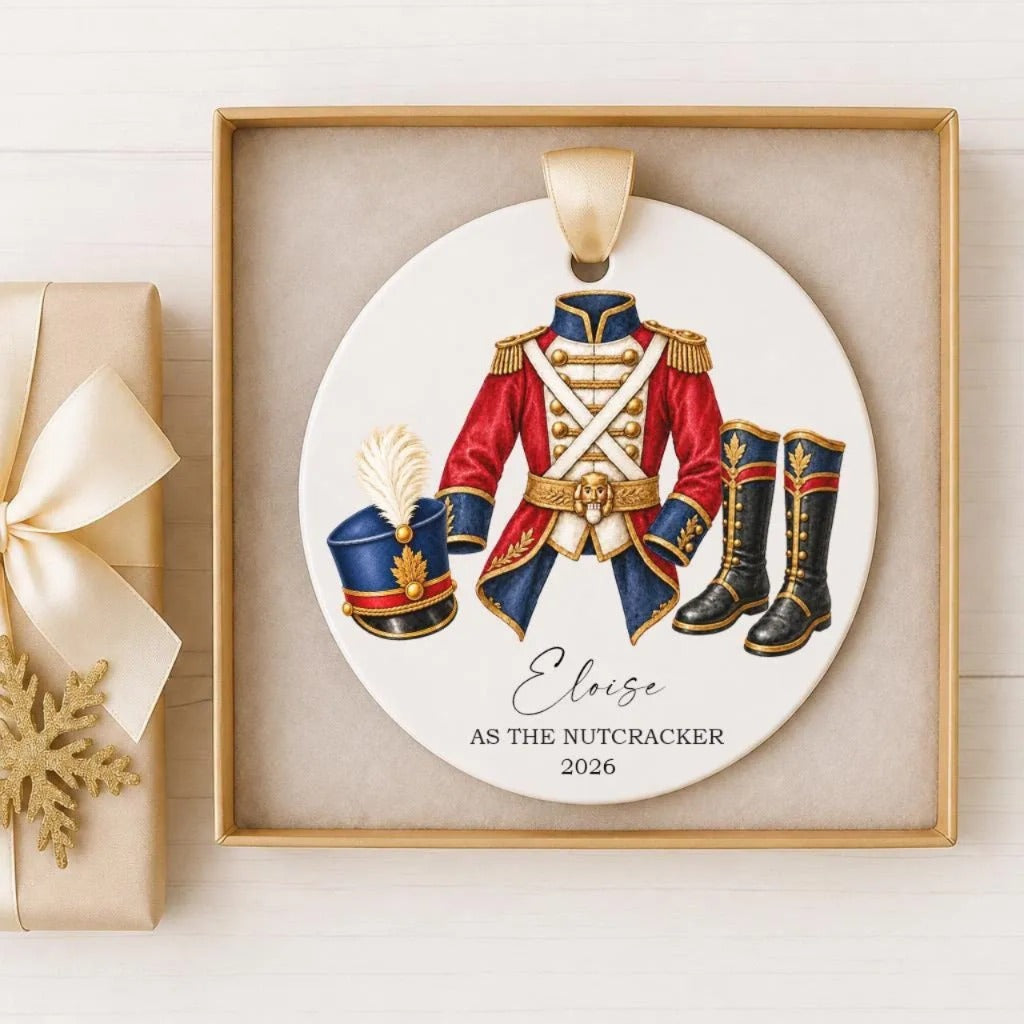 A decorative ornament featuring a red and blue military uniform, a hat, and boots, with the text "Elise as the Nutcracker" and the year "2026" below it.