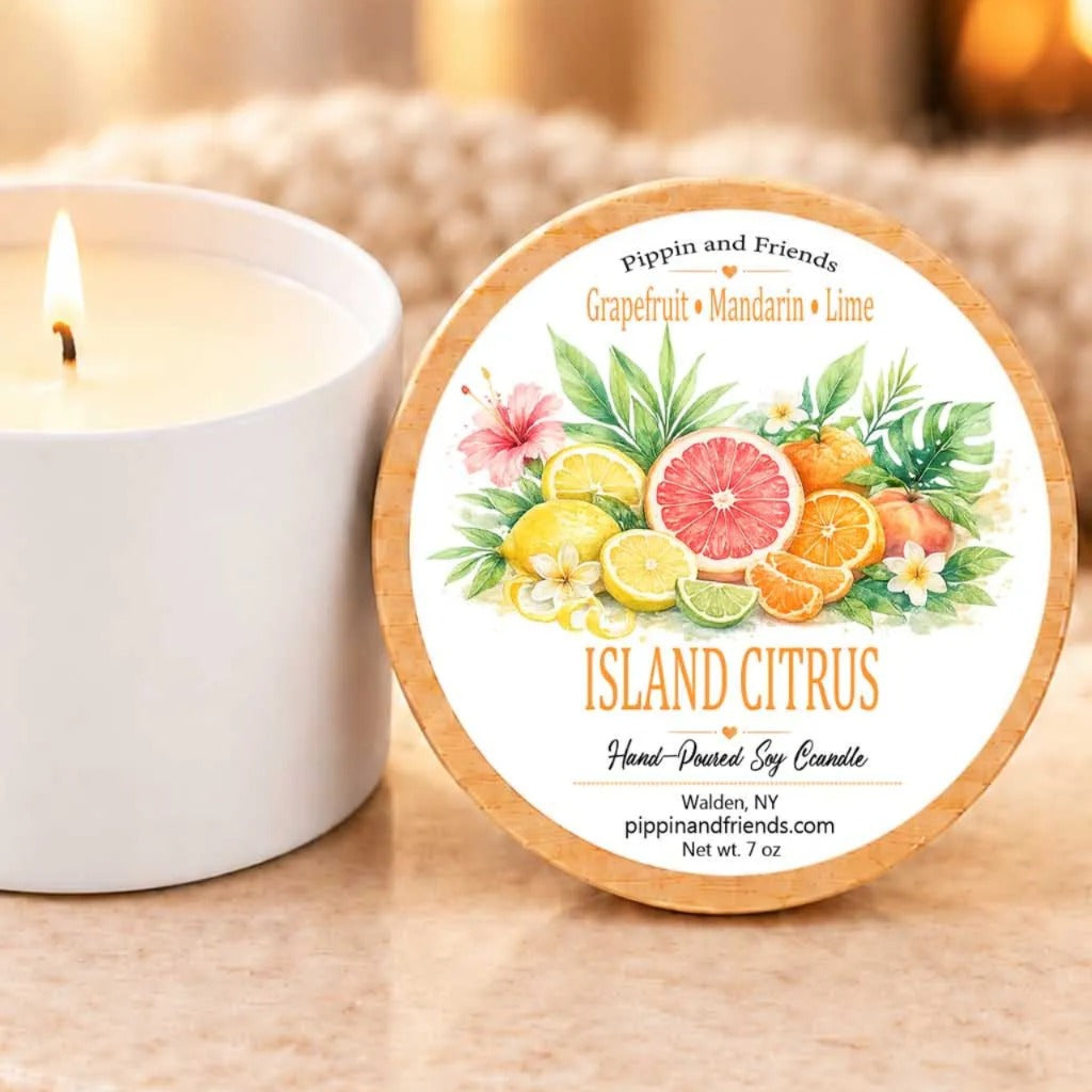 A white candle with a label that reads "Island Citrus" next to a lit candle on a table.