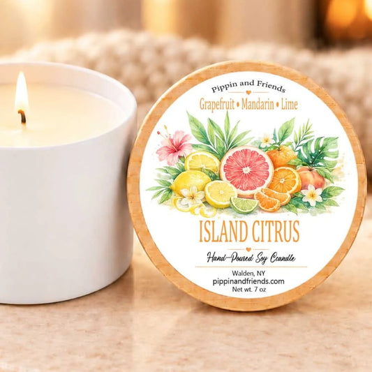 A white candle with a label that reads "Island Citrus" next to a lit candle on a table.