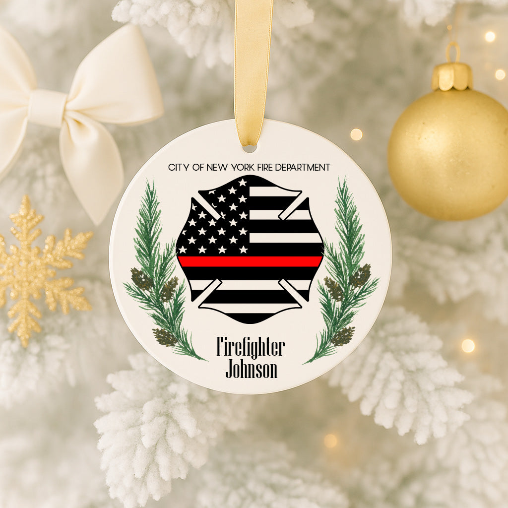 A white ornament with a black and red striped design, featuring a firefighter's helmet and a ribbon, hangs on a Christmas tree.