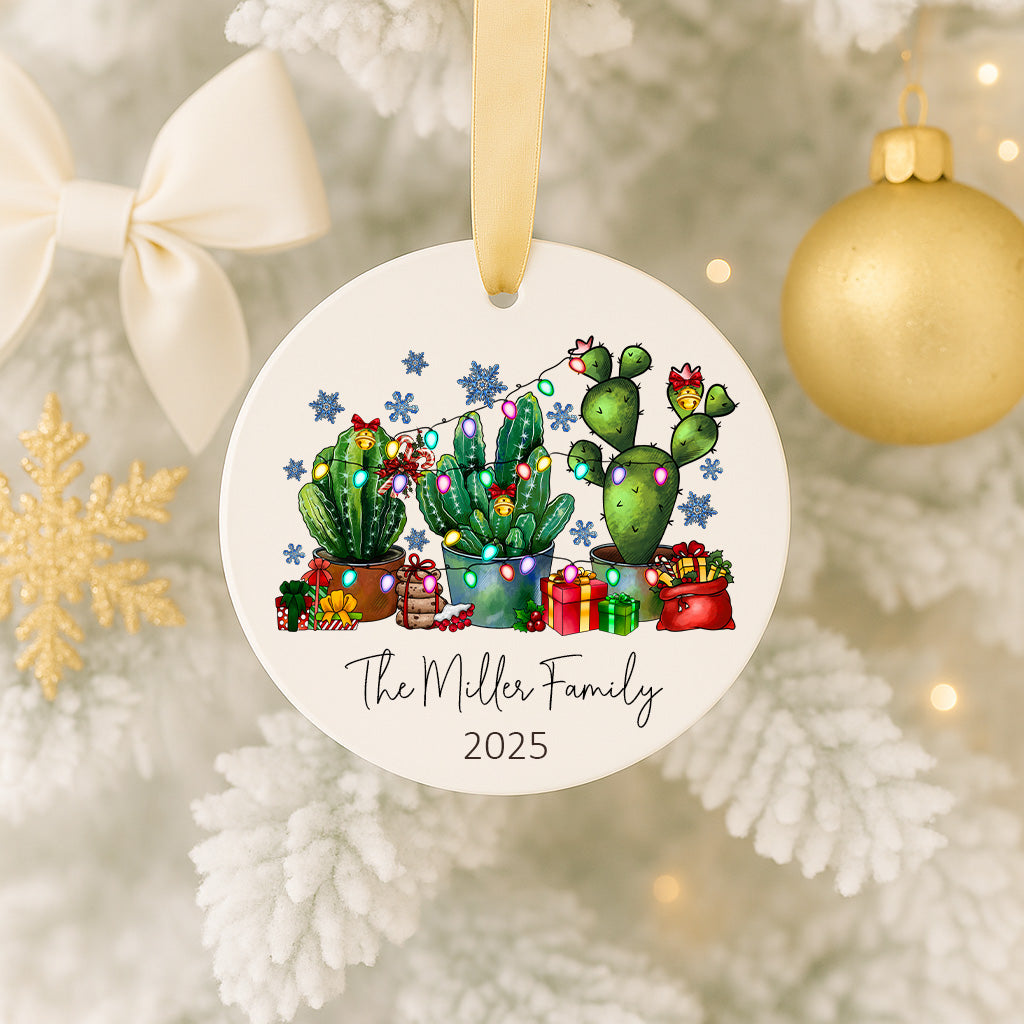 A white ornament with a festive design featuring cacti and Christmas lights, hanging on a tree.