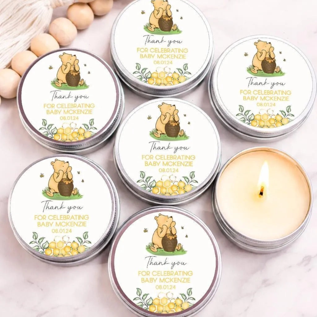 a collection of round tin candles with labels that read "Thank you for celebrating Baby McKenzie" and "08/01/14". The candles are arranged on a marble surface, with some of them lit.