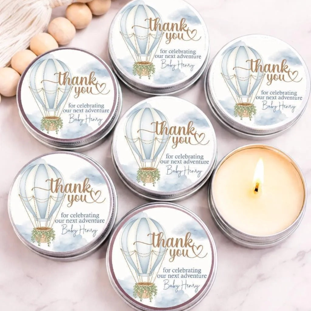 a collection of round tin candles with a white and blue design, along with a few wooden beads. The candles are arranged on a marble surface, and there is a lit candle in one of the tin candles.