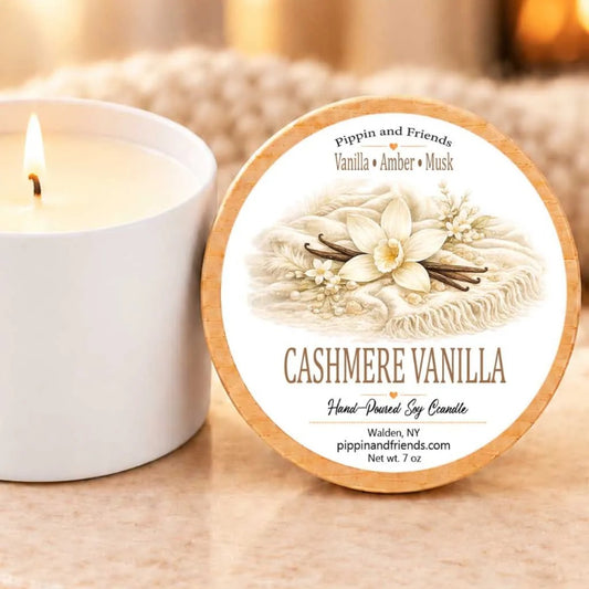 a white candle labeled "CASHMERE VANILLA" next to a white candle, both sitting on a table.