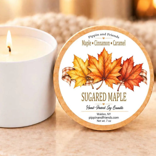 A white candle with a label featuring autumn leaves and the text "SUGARED MAPLE Hand-Poured Soy Candle" next to it.