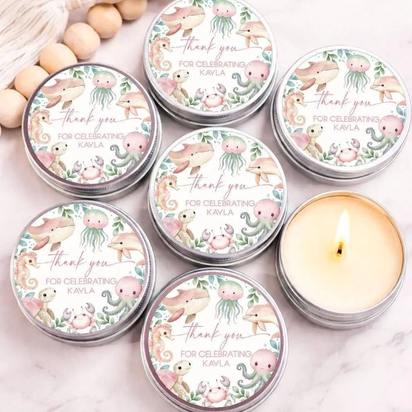 Under the sea baby shower candle favors with personalized ocean animal labels in silver tins displayed on marble background.