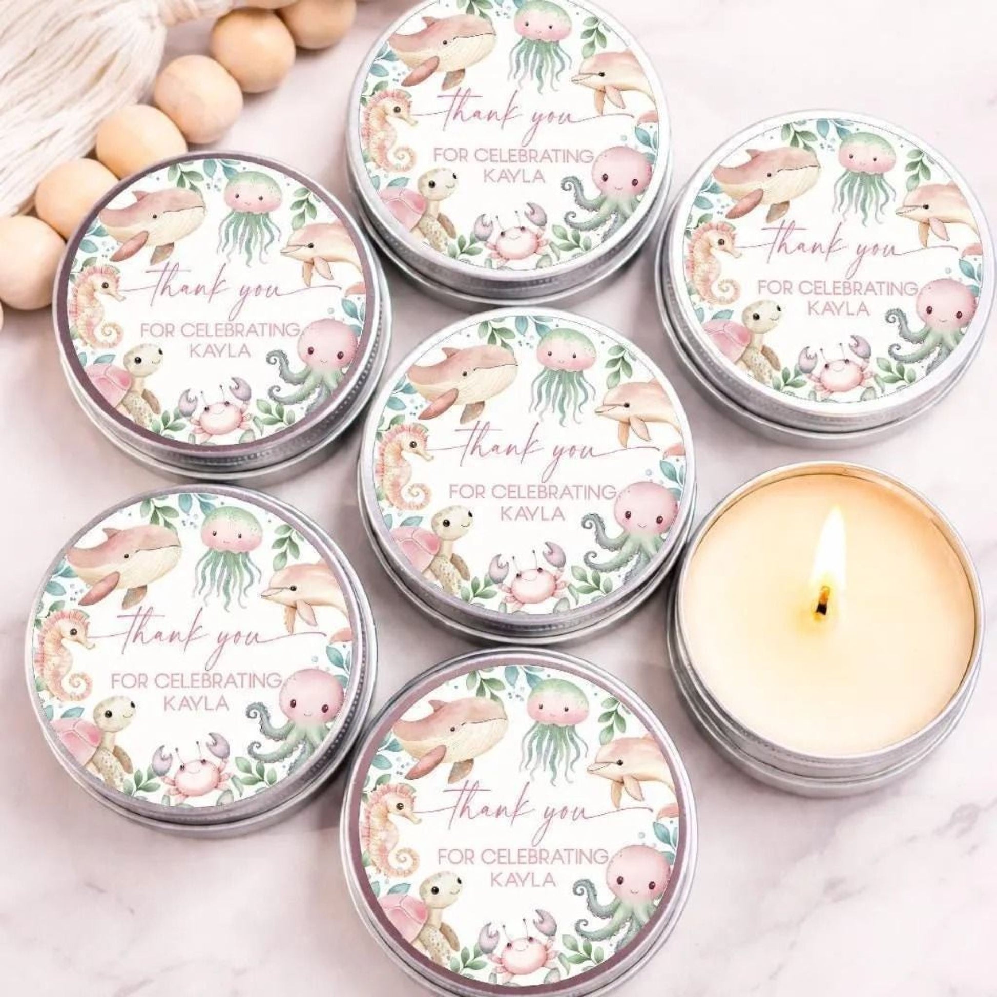 Under the sea baby shower candle favors with personalized ocean animal labels in silver tins displayed on marble background.