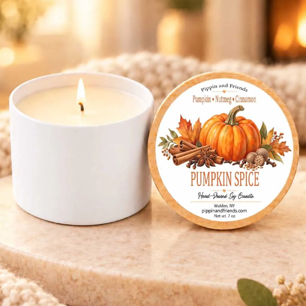 A white candle with a pumpkin and cinnamon scent is placed next to its lid, which features an illustration of a pumpkin and cinnamon.