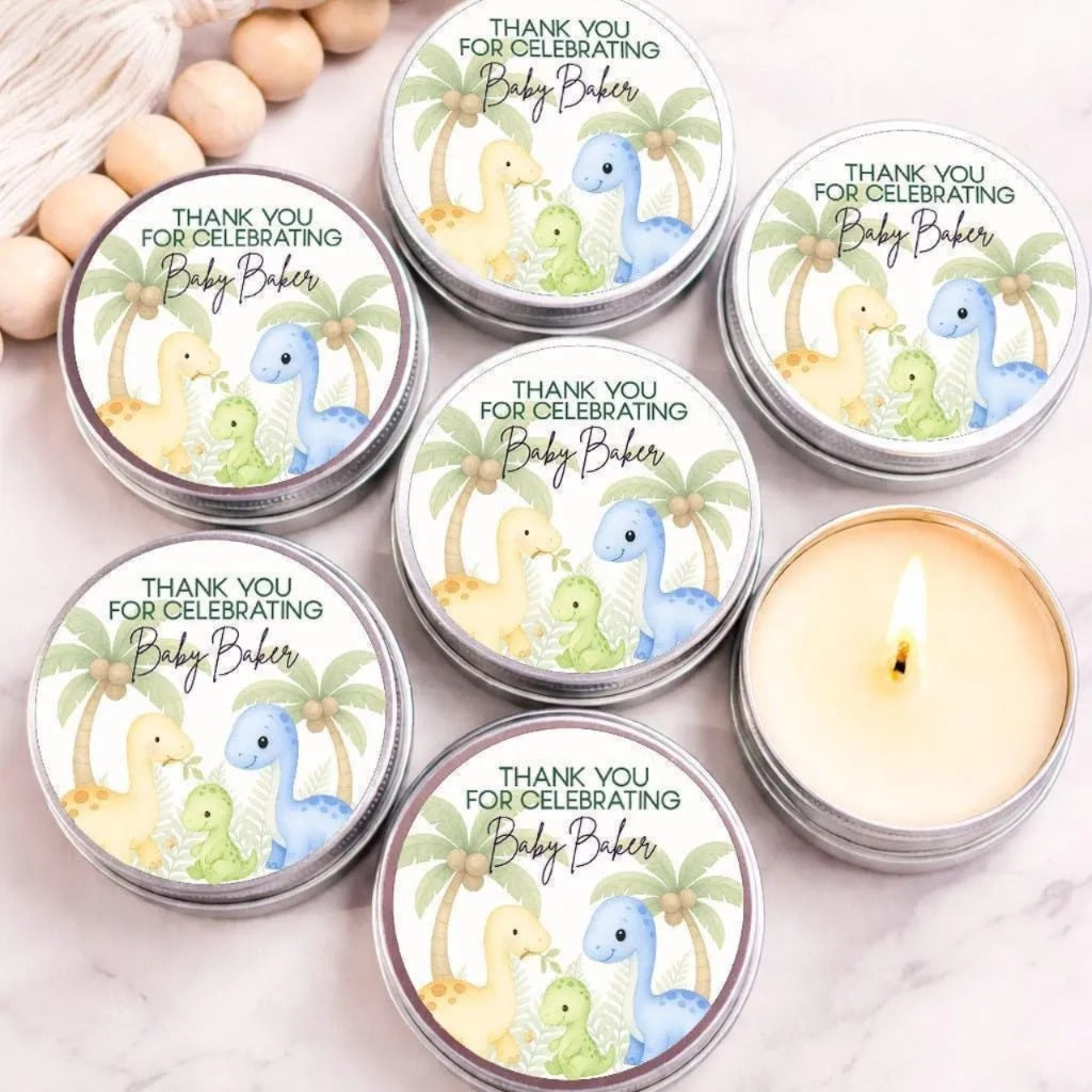 a collection of round tin candles with labels that read "Thank you for celebrating Baby Baker" and feature illustrations of dinosaurs.