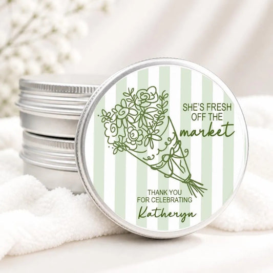 A round tin lid with a green floral design and text on it, placed on a white cloth.