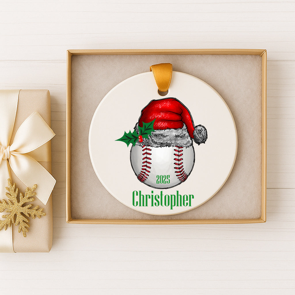 A white ornament with a baseball and Santa hat design, and the name "Christopher" written on it, is displayed in a box.