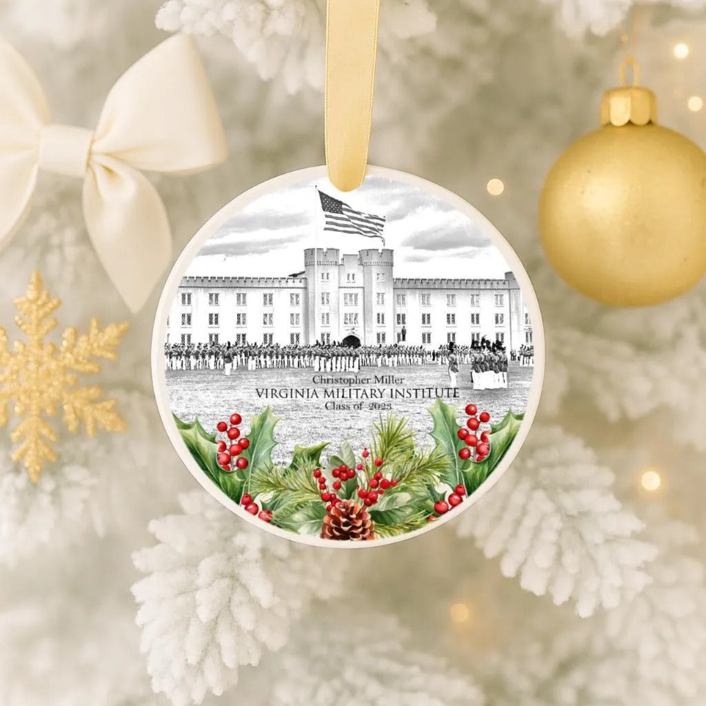 A round ornament featuring a drawing of a building with a flag, surrounded by holly, berries, and pine cones, hanging on a Christmas tree.