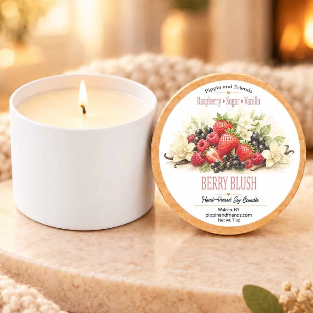 A white candle labeled "Berry Blush" sits next to a white candle, both placed on a wooden surface.