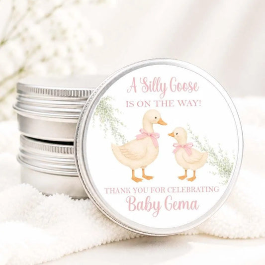 A round tin can with a label featuring illustrations of two ducks and text that reads "A Silly Goose is on the way! Thank you for celebrating Baby Gema".