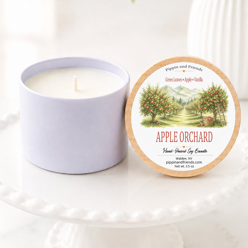 Apple harvest soy candle in a white ceramic vessel with a natural wood lid featuring a watercolor apple orchard label, hand-poured by Pippin and Friends