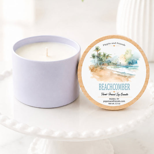A soy candle in a white ceramic vessel with a natural wood lid featuring a watercolor beach label, hand-poured by Pippin and Friends