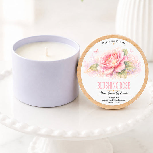 A soy candle in a white ceramic vessel with a natural wood lid featuring a watercolor pink rose label, hand-poured by Pippin and Friends