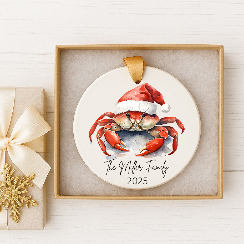 A white ornament with a red crab wearing a Santa hat, placed in a gold frame.