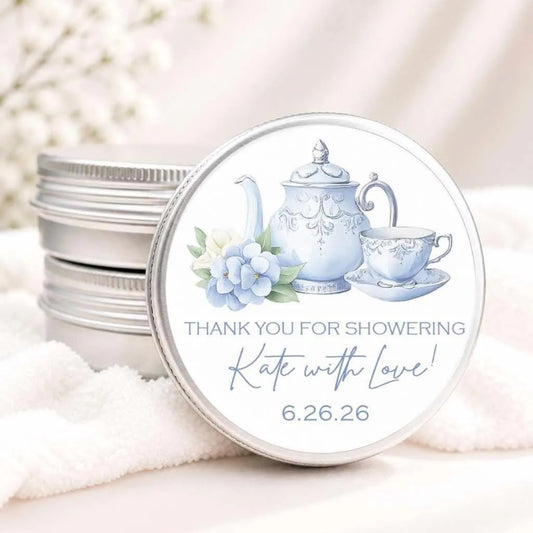 A round tin lid with a teapot and teacup illustration, along with a message that says "Thank you for showering Kate with love! 6.26.26".