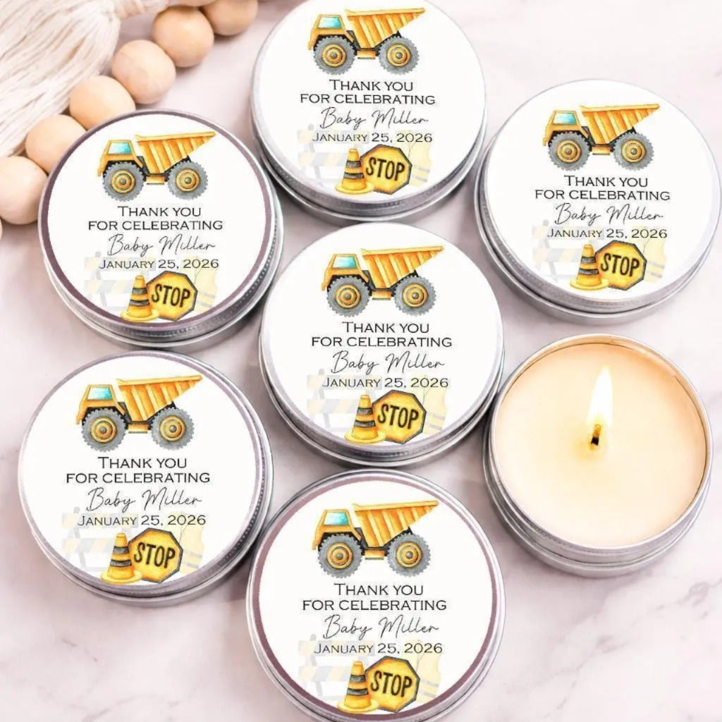 six silver tin candles with white labels, each featuring an illustration of a yellow dump truck and the text "Thank you for celebrating Baby Miller January 25, 2026".