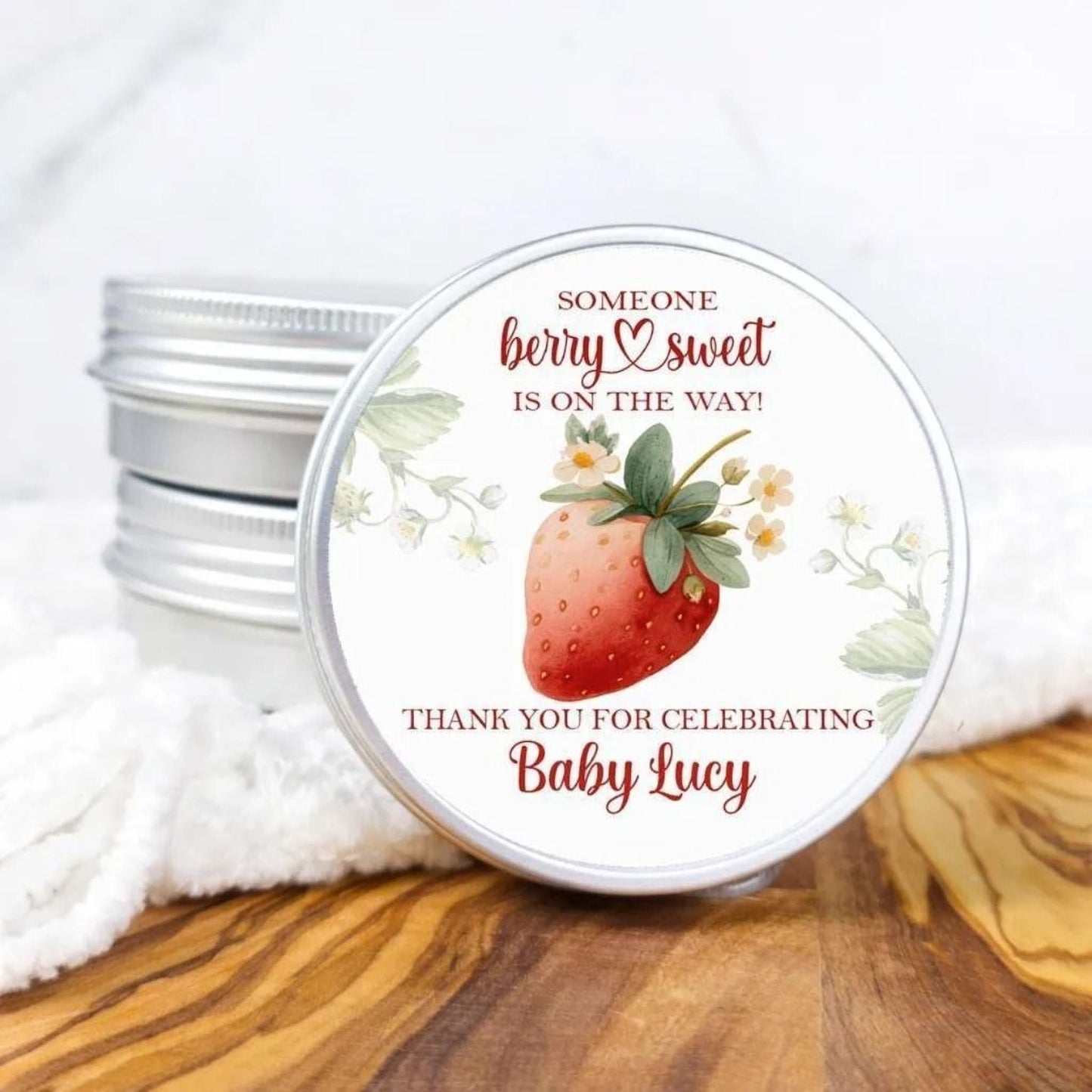 A round tin lid with a strawberry design and text, placed on a wooden surface.