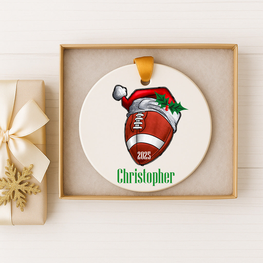 A personalized Christmas ornament featuring a football with a Santa hat and the name "Christopher" below it, displayed in a box.