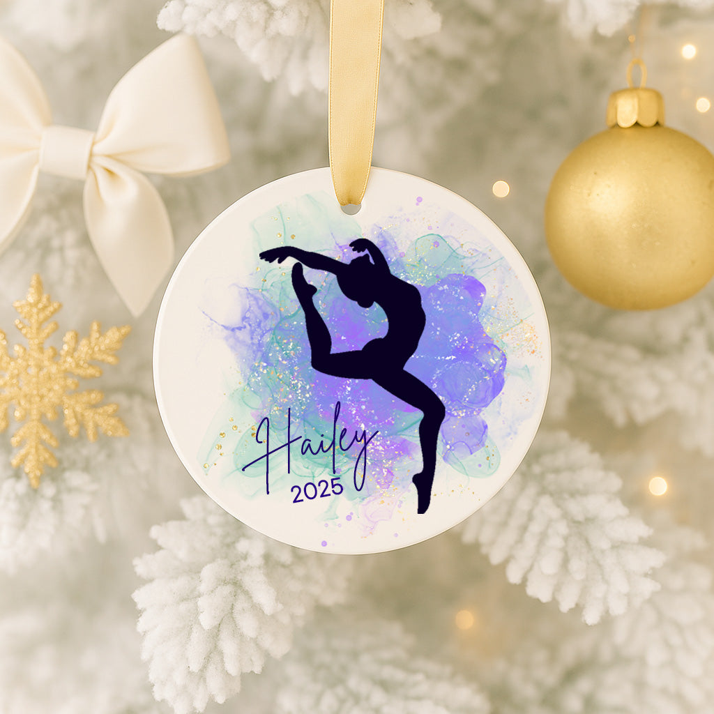 A white ornament with a purple and blue abstract design, featuring a silhouette of a person in a dynamic pose, is hanging on a Christmas tree.