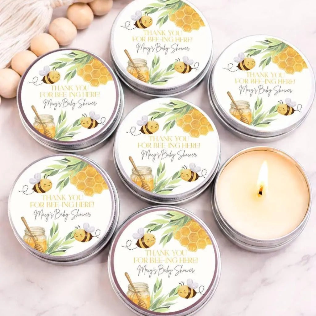 six silver tins with a honeycomb and bee design, arranged on a marble surface. Each tin has a label that reads "Thank you for being here! May's Baby shower" along with illustrations of bees and honeycombs.