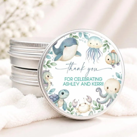 A round tin lid with a decorative design featuring various sea creatures, such as a whale, jellyfish, and octopus, along with the text "Thank you for celebrating Ashley and Kerr!"